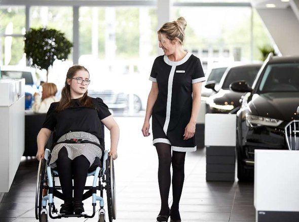 A young wheelchair user next to an adult in a car showroom